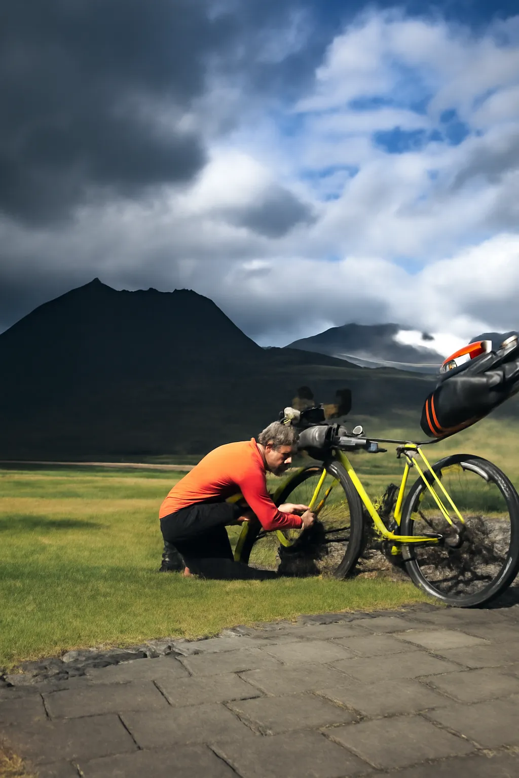 Cicloturista ajustando a bicicleta em uma paisagem montanhosa